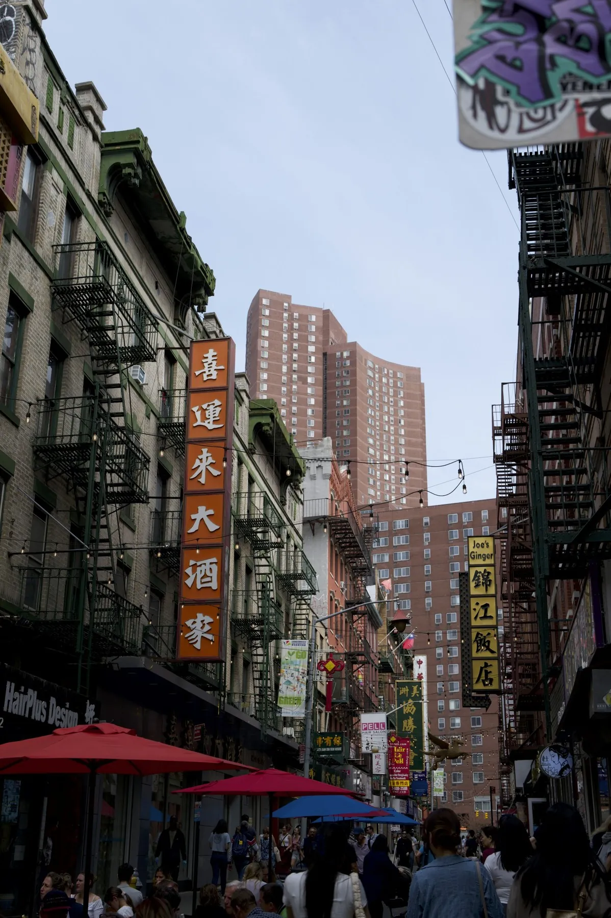Chinatown street with fire escapes, orange and yellow vertical signs and colorful sidewalk umbrellas
